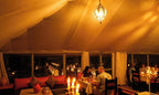 Merzouga Desert Camp cozy dining area with warm amber lighting, candlelit tables, red cushions, and traditional decor
