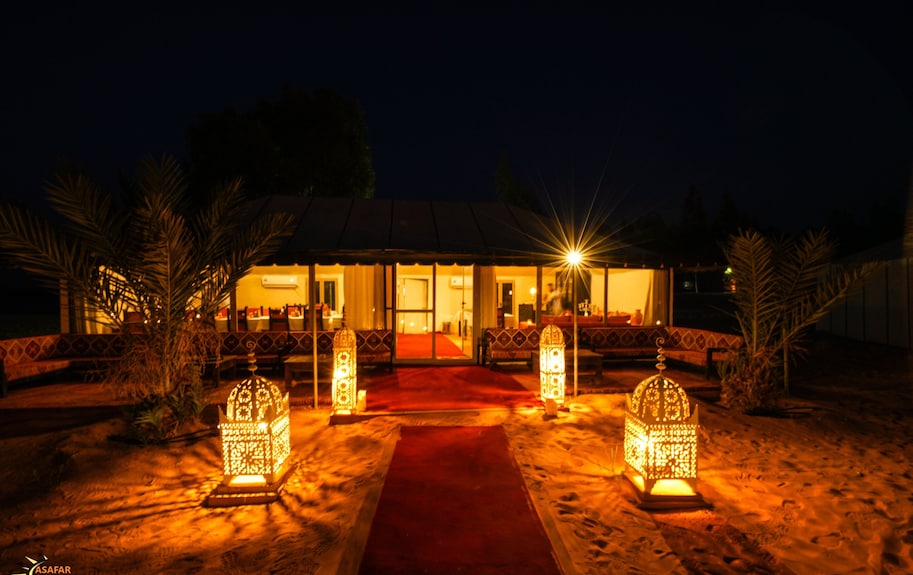 Merzouga Desert Camp illuminated at night with traditional Moroccan lanterns, red carpet, and desert surroundings