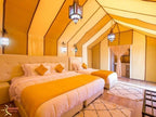 Merzouga Desert Camp luxury tent interior with two beds, yellow and white decor, ethnic-patterned rugs, and lantern lighting
