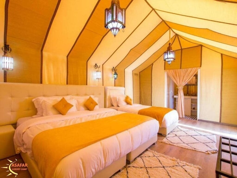 Merzouga Desert Camp luxury tent interior with two beds, yellow and white decor, ethnic-patterned rugs, and lantern lighting