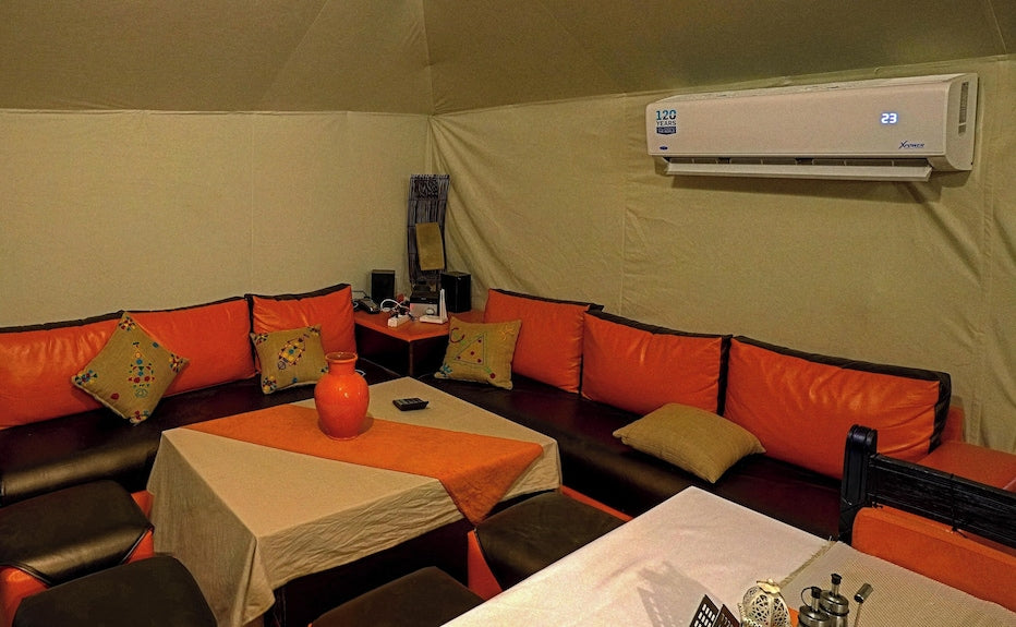 Merzouga Desert Camp interior featuring orange and brown cushioned corner seating, beige tablecloth with orange runner and decorative vase