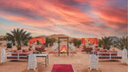 Merzouga Desert Camp outdoor seating area with traditional lanterns, red canopies, patterned cushions, and a central fire pit at sunset