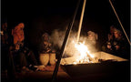 Merzouga Dinner showing a group of men in traditional Berber clothing sitting around a desert campfire playing drums and castanets at night