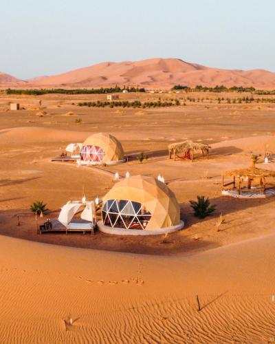 Merzouga Glamping Camp with beige geodesic dome tents featuring glass windows set in the Sahara Desert sand dunes.