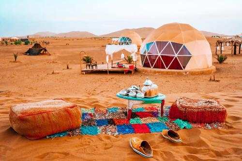 Merzouga Glamping Camp featuring dome tents in the Sahara Desert with colorful rugs, low seating, and traditional tea set.