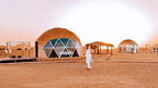 Merzouga Glamping Camp featuring beige dome tents with large glass windows and traditional shade structures in the desert.