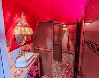 Bathroom interior with a white sink, decorative mirror, and tiled floor inside a red canvas tent at Merzouga Glamping Camp.