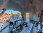 Merzouga Glamping Camp interior featuring a spacious beige tent with large windows, wooden floor, cozy seating, and desert views.