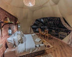 Merzouga Glamping Camp featuring a spacious beige tent interior with a large bed, Moroccan decor, and wooden flooring.