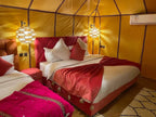 Luxury Merzouga Glamping Camp bedroom with mustard yellow tent walls, red and pink bedding, cozy pillows, and hanging lamps.