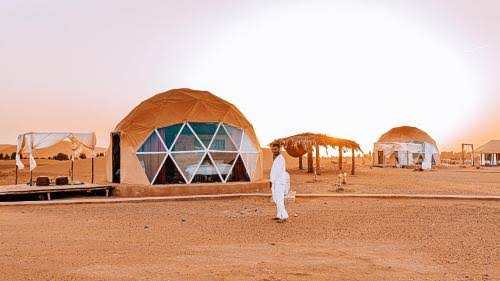 Merzouga Glamping Camp featuring dome-shaped beige tents with geometric glass panels and traditional desert decor under a clear sky.