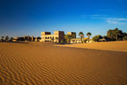 Merzouga hotel kanz Erremal sandy desert landscape with traditional Moroccan architecture and palm trees under a clear sky