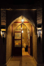 Entrance doorway of Merzouga hotel kanz Erremal with arched design, textured walls, warm lighting, and traditional lanterns