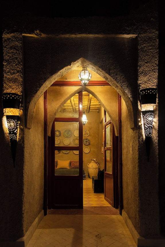 Entrance doorway of Merzouga hotel kanz Erremal with arched design, textured walls, warm lighting, and traditional lanterns