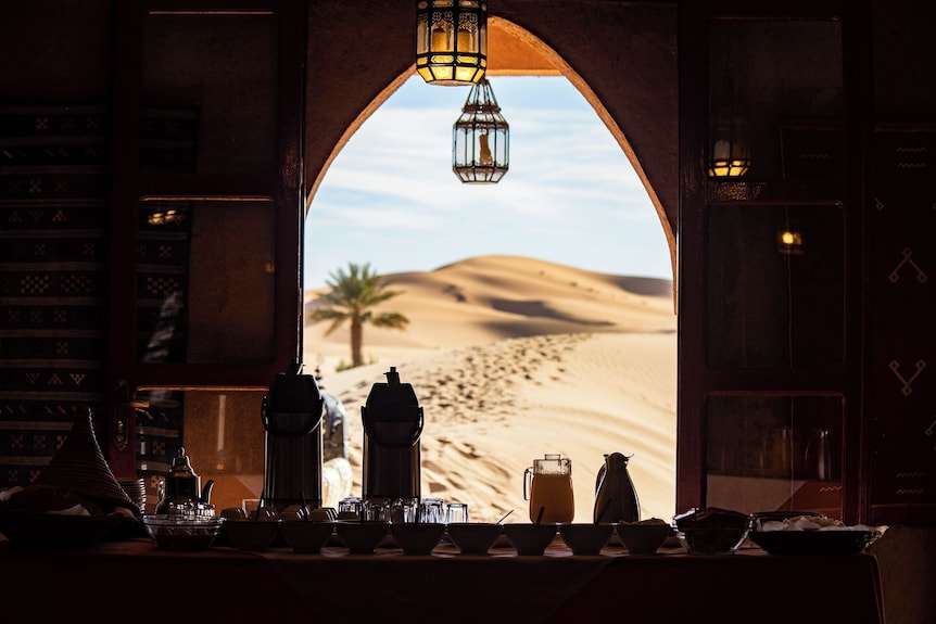Merzouga hotel kanz Erremal traditional Moroccan desert room with arched doorway overlooking sand dunes and palm tree