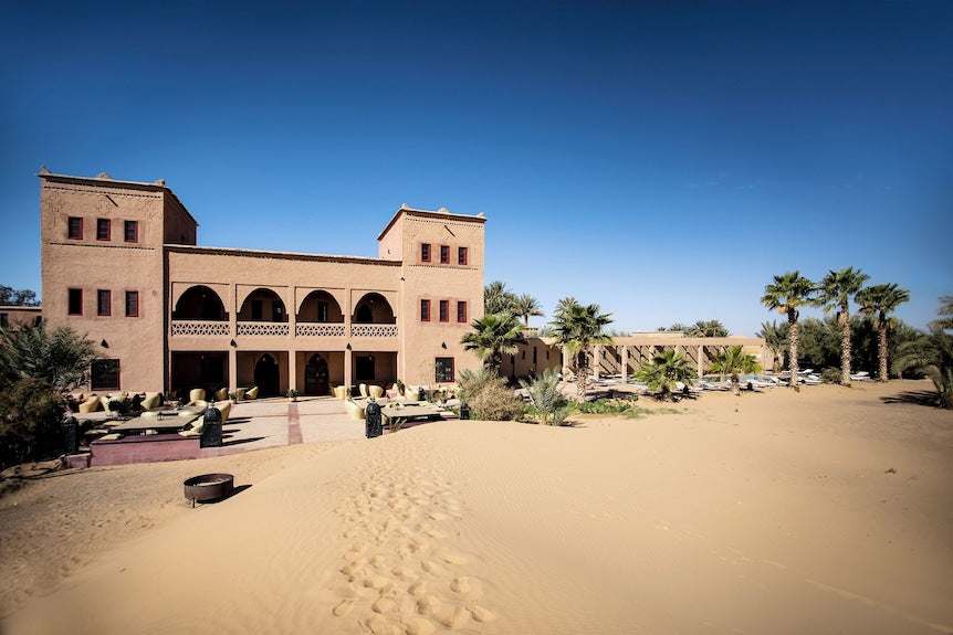 Merzouga hotel kanz Erremal traditional mud brick building with arched balconies and surrounding desert sand dunes
