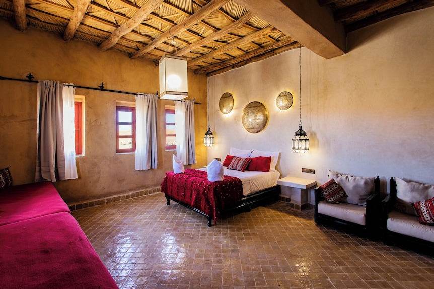 Merzouga hotel kanz Erremal room with red bedding, rustic beige walls, woven ceiling, and traditional Moroccan decor