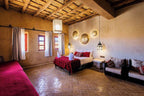 Merzouga hotel kanz Erremal room with red bedding, rustic beige walls, woven ceiling, and traditional Moroccan decor