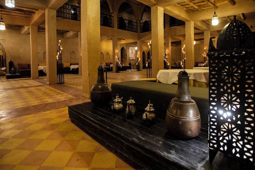 Traditional Moroccan hotel interior at Merzouga hotel kanz Erremal with rustic yellow pillars, tiled floor, and decorative lanterns