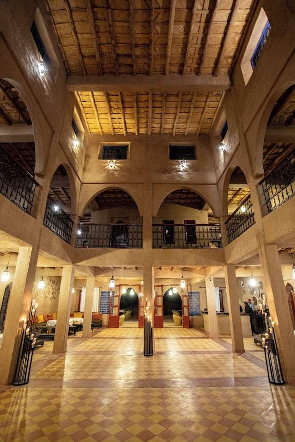 Spacious lobby of Merzouga hotel kanz Erremal featuring traditional Moroccan architecture, wooden ceiling, arches, and warm lighting