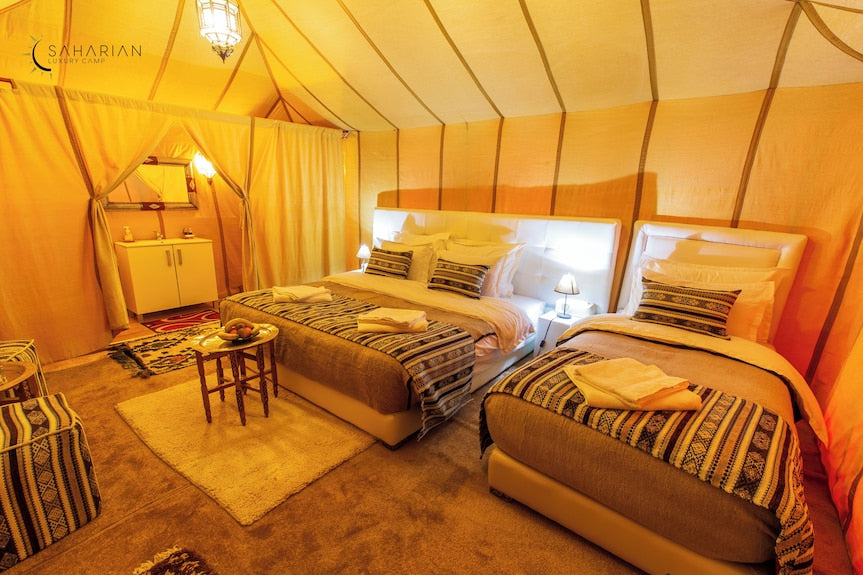 Merzouga Luxury Camp interior with beige fabric tent, twin beds featuring patterned bed runners and soft lighting