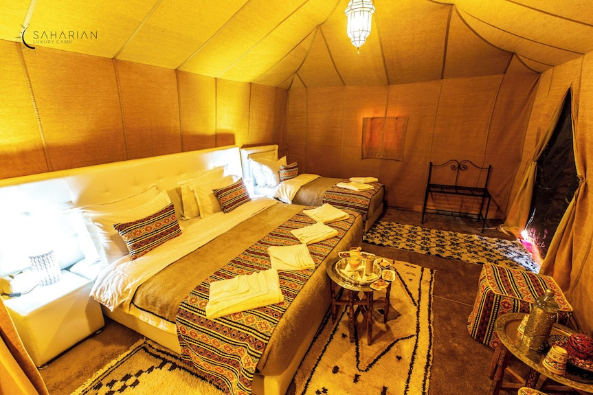 Merzouga Luxury Camp interior with cozy double and single beds, traditional patterned textiles, warm lighting, and rustic carpet