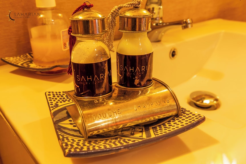 Merzouga Luxury Camp branded black and white gel and shampoo bottles on a decorative ceramic plate in a bathroom sink