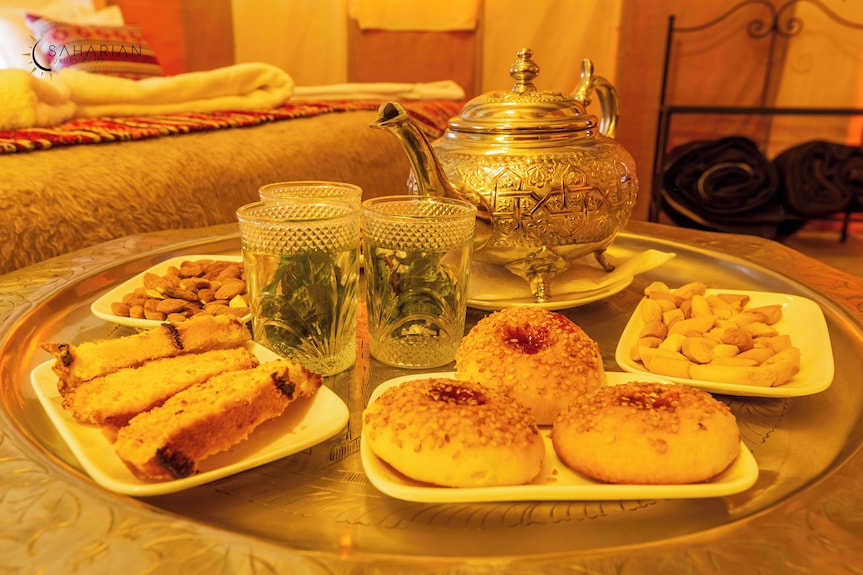 Merzouga Luxury Camp traditional Moroccan tea set with ornate teapot, two glasses of mint tea, and assorted pastries on silver tray
