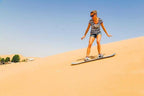 Merzouga Luxury Camp desert sandboarder wearing striped shirt and shorts riding down golden dune under clear sky
