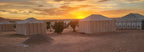 Merzouga Luxury Camp at sunset featuring white desert tents with vertical stripes and a sandy landscape with sparse vegetation