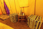 Merzouga Luxury Camp interior with yellow fabric walls, patterned ottomans, small wooden table, and traditional desert decor