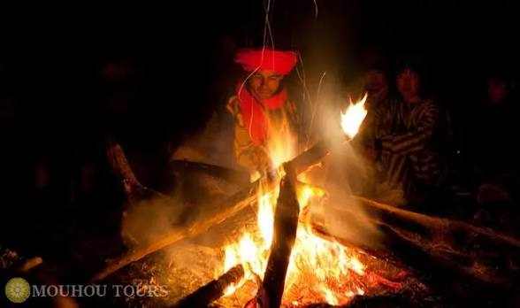 Campfire with glowing orange flames surrounded by people in traditional clothing, highlighting the warmth of a Merzouga Overnight Luxury Sahara Desert Camp experience.