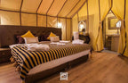 Luxury desert tent interior featuring a large bed with black and yellow striped blanket and tan curtains at Merzouga Overnight Luxury Sahara Desert Camp.