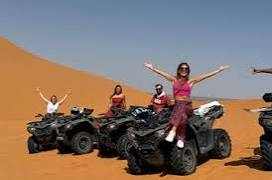 Merzouga Quad Bike adventure with riders on black quad bikes in orange desert sand dunes under clear blue sky