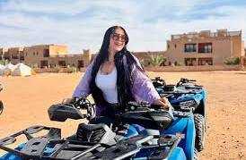 Merzouga Quad Bike in bright blue with black accents parked in desert sand beside a woman wearing sunglasses and a lavender jacket