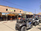 Merzouga Quad Bike parked on a street, featuring black and blue colors with rugged tires and storage compartments