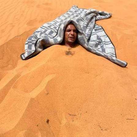 Man covered in warm golden desert sand with a gray patterned blanket over his head during Merzouga Sand Baths therapy session