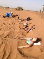Merzouga Sand Baths featuring people partially buried in warm golden desert sand with heads uncovered under clear sky