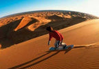 Merzouga Sandboarding featuring a person in red jacket and white pants sliding down golden sand dunes in the Sahara Desert