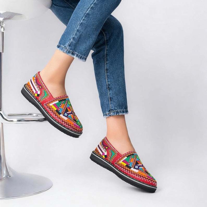 Moroccan Berber leather moccasins in vibrant red with multicolored embroidered patterns and black soles, perfect for Merzouga Shopping.
