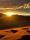 Sunset over golden sand dunes with dramatic cloud patterns highlighting the Merzouga Sunset Camel Trekking landscape.
