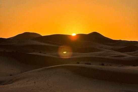 Sunset over golden sand dunes in the Sahara desert with rolling hills of warm orange and brown tones, perfect for Merzouga Sunset Camel Trekking.