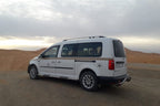 White passenger van parked on desert terrain with sandy dunes in the background, ideal for Merzouga Taxi Rent