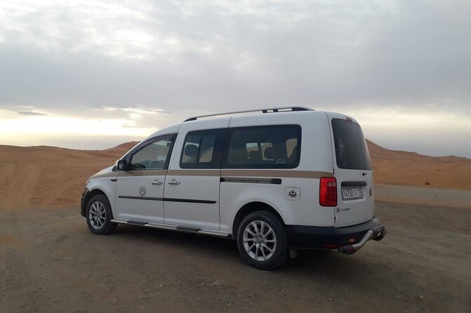 White passenger van parked on desert terrain with sandy dunes in the background, ideal for Merzouga Taxi Rent