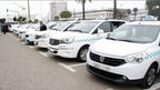 White taxis with blue checkered stripes parked in a row with drivers nearby, representing Merzouga Taxi Rent services