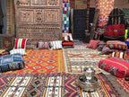 Traditional Moroccan rugs and cushions in various vibrant colors and geometric patterns with a metal tea set on a tray, evoking Merzouga to Fes cultural style