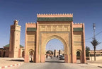 ornate historic sandstone arch gate with green tiled roofs and intricate patterns in Morocco under clear blue sky