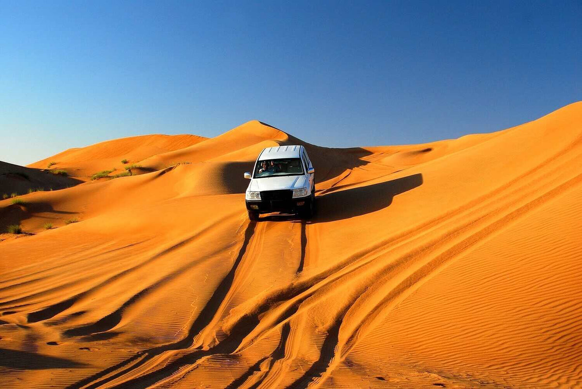 White 4x4 vehicle driving on vibrant orange sand dunes in the desert, highlighting an adventurous Merzouga to Zagora tour.