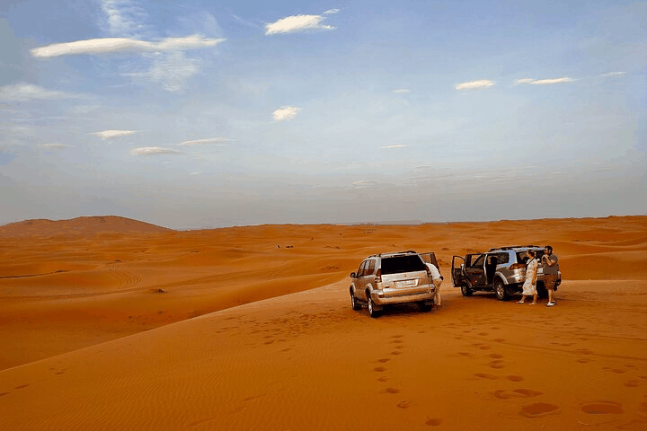 4x4 SUVs in silver and black parked on golden sand dunes with footsteps nearby during Merzouga to Zagora desert tour