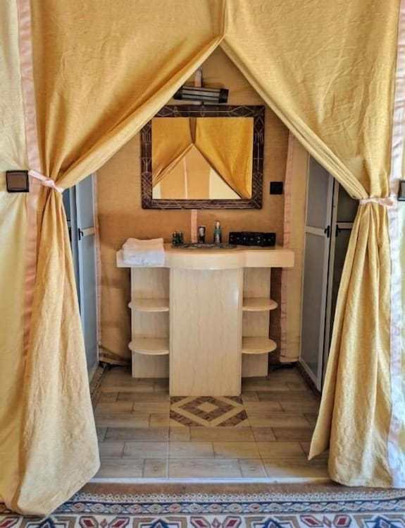 Merzouga VIP Luxury Camp bathroom area with beige curtains, a cream vanity sink, tiled floor, and a framed mirror